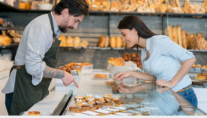woman talking to baker and pointing at a selection of pastry